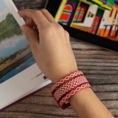 a person is holding an open book and wearing a red bracelet with white braiding