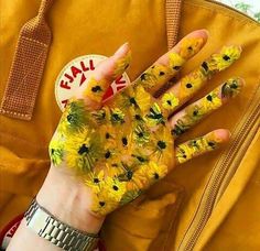 a person's hand with yellow flowers painted on it and a suitcase in the background