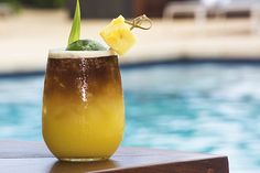 a drink with a pineapple garnish on the rim next to a pool