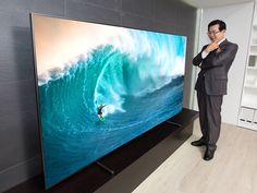 a man standing in front of a large screen tv with a surfer on it's side