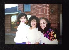 three women are posing for a photo in front of a house