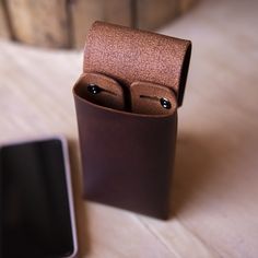 a cell phone sitting next to a leather case on top of a wooden table,