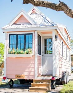 a tiny pink house on wheels parked in front of a tree with flowers growing out of the windows