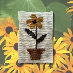 a crocheted flower pot holder with yellow flowers in front of sunflowers