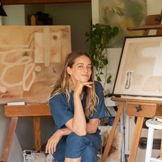 a woman is sitting in front of an easel with her hand on her chin