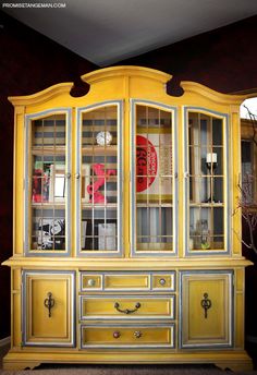 a yellow china cabinet with glass doors and drawers