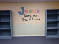 two blue bookshelves in front of a wall painted with the words jesus loves me, this i know