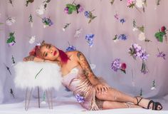 a woman with red hair and tattoos sitting on a white chair in front of flowers