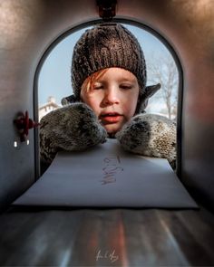 a young boy wearing a knitted hat and mittens looking through an opening in a tunnel