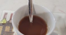 a spoon sticking out of a coffee cup filled with liquid on top of a table