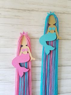 two paper cutouts of mermaids are hanging on the wall