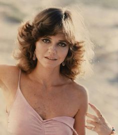 the woman is posing on the beach with her hand in her hair and wearing a pink top