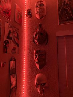 several masks are hanging on the wall with red light coming from behind them in a dark room