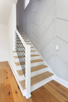 an empty room with wood floors and white painted walls, along with wooden stairs leading up to the second floor