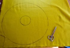 a pair of scissors sitting on top of a yellow piece of fabric with a circle drawn in it