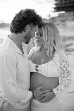 a pregnant couple cuddles on the beach for their black and white photo session