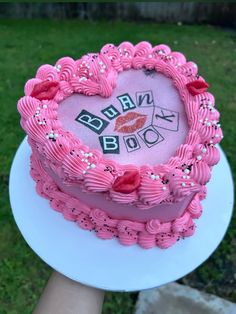 a pink heart shaped cake sitting on top of a white plate in front of a green lawn