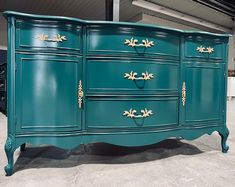 a blue dresser with gold trim and handles on it's sides, in a warehouse