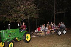 a group of people riding on the back of a green tractor in front of trees