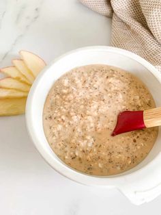 a white bowl filled with oatmeal next to an apple and cinnamon stick