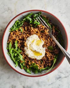 a bowl filled with rice, greens and an egg on top of it next to a fork