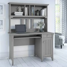 a computer desk with a laptop and bookshelf in the corner, next to a window