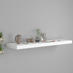 two white shelves with plants and cups on them, one shelf has a plant in it