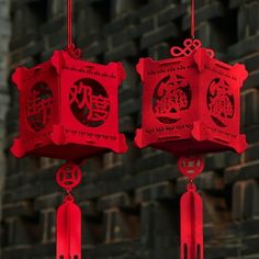 two red lanterns with chinese writing on them hanging from strings in front of a brick wall