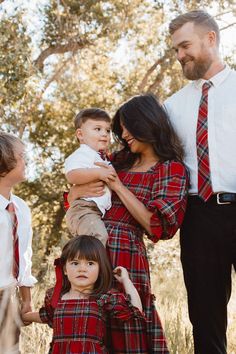 a family poses for a photo while wearing ties and dress clothes in the woods with trees behind them