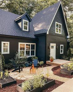 a black house with lots of windows and plants in the front garden area, surrounded by trees