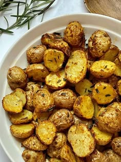 a white plate topped with cooked potatoes next to a wooden spoon and rosemary sprigs