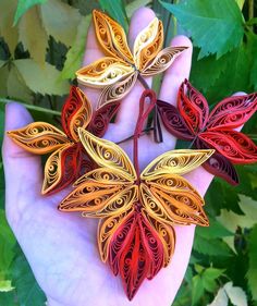 the hand is holding four different colored paper butterflies in it's palm, with green leaves behind them