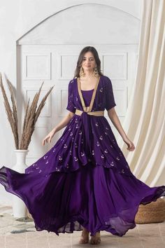 Strut around in this contemporary style indo-western dress in deep amethyst hue with contrasting golden handwork. Designed with eye-catching floral motifs and a wrapped silhouette, this dress has the required sophistication and charm. With a deep V neck and knotted appeal, style it with layered necklace and earrings for an event-ready ensemble you'll adore.Style Wrap style dress Knotted closure Ankle length style Embroidered lace detailing All over motif embroidery Decadent amethyst color George Purple Formal Sets For Diwali, Formal Purple Sets With Zari Work, Eid Georgette Dress With Front Open, Purple Formal Sets With Traditional Drape, Formal Purple Sets With Traditional Drape, Semi-stitched Front Open Dress For Festive Occasions, Front Open Georgette Dress With Dupatta, Semi-stitched Purple Formal Dress, Front Open Dress With Zari Work For Reception