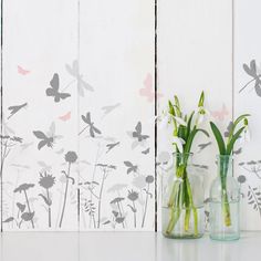 three glass vases with flowers in them on a white countertop against a painted wall