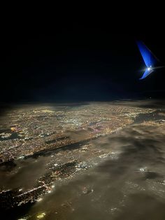 an airplane wing flying over the city lights at night in the sky above the clouds