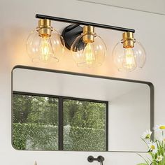 a bathroom vanity with three lights and a mirror above it, in front of a window