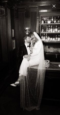 black and white photograph of bride and groom kissing in front of shelves with liquor bottles