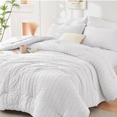 a bed with white comforter and pillows on top of it in a room next to a potted plant