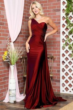 a woman standing in front of a brick wall wearing a long red dress with one shoulder