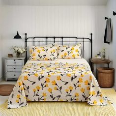 a bed with yellow flowers on it in a white and black bedroom, next to an iron headboard