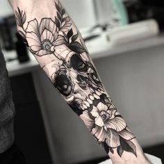 a person with a tattoo on their arm that has flowers and a skull in it