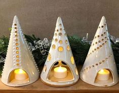 three white ceramic candlesticks sitting on top of a wooden shelf next to christmas greenery