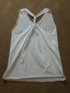 a white tank top with a knot on the front and back side, laying on a carpeted floor