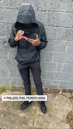 a person wearing a black jacket and pants standing in front of a brick wall with the words philadelphia pennsylvania written on it