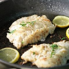 two fish fillets in a skillet with lemon slices