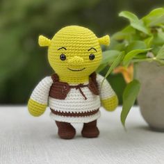 a crocheted toy is standing next to a potted plant