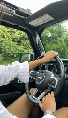 a woman driving a car with her hands on the steering wheel, and trees in the background