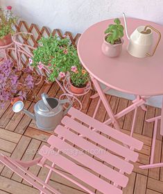 a pink table and chairs on a wooden deck with potted plants in the background