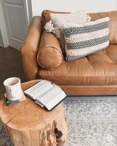 a coffee table with an open book and cup on it next to a leather couch