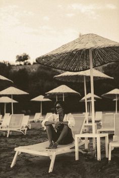 a woman sitting on a beach chair under an umbrella